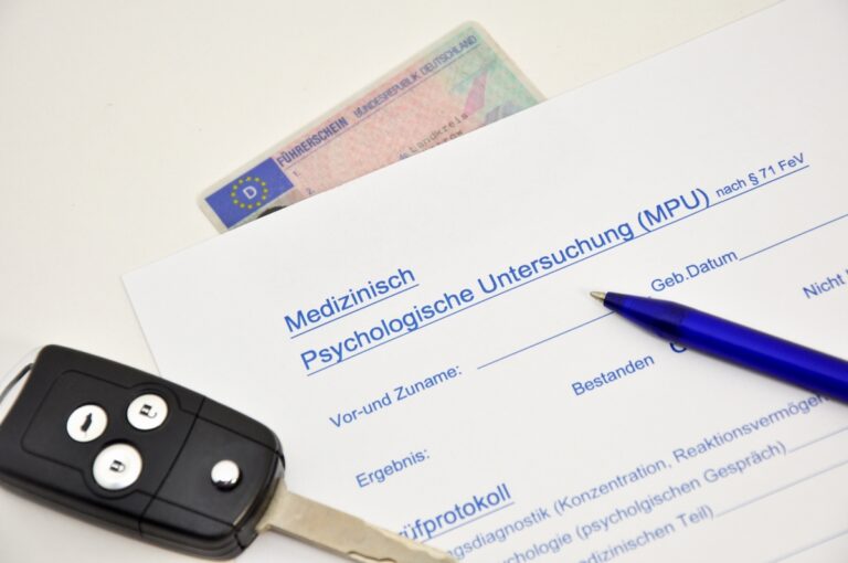 Ein Formular zur MPU, ein Führerschein, ein Autoschlüssel und ein Stift liegen auf einem weißen Tisch.